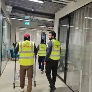 Workers in high-visibility vests moving through an office corridor with a trolley – representing professional office relocation services