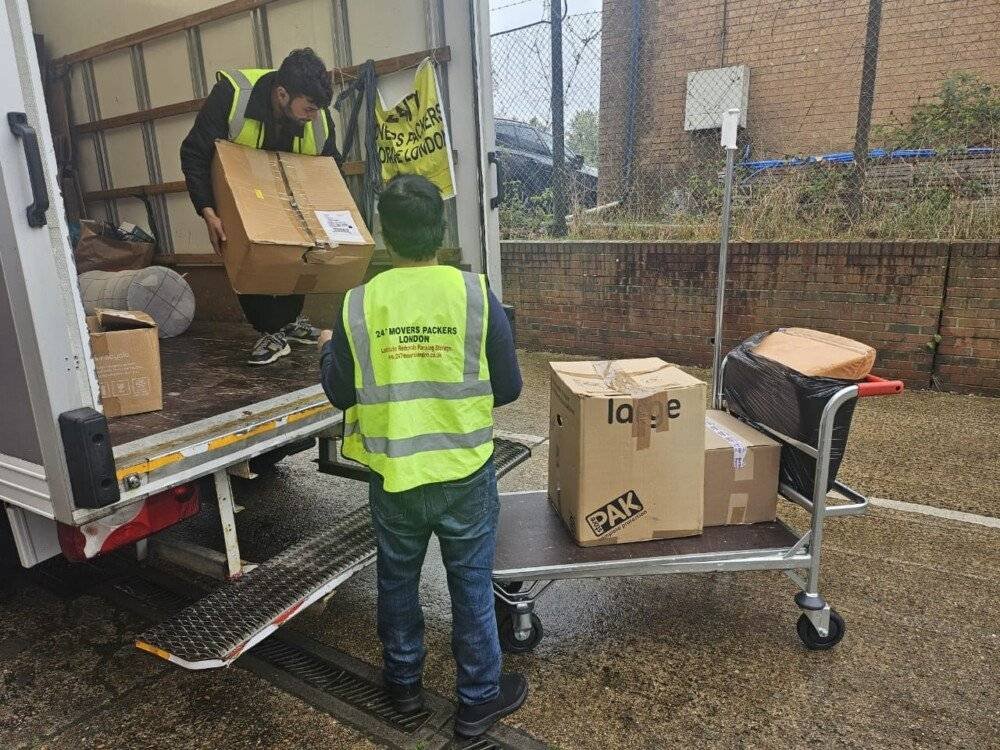 Two man are unloading the boxes from the truck in the trolley