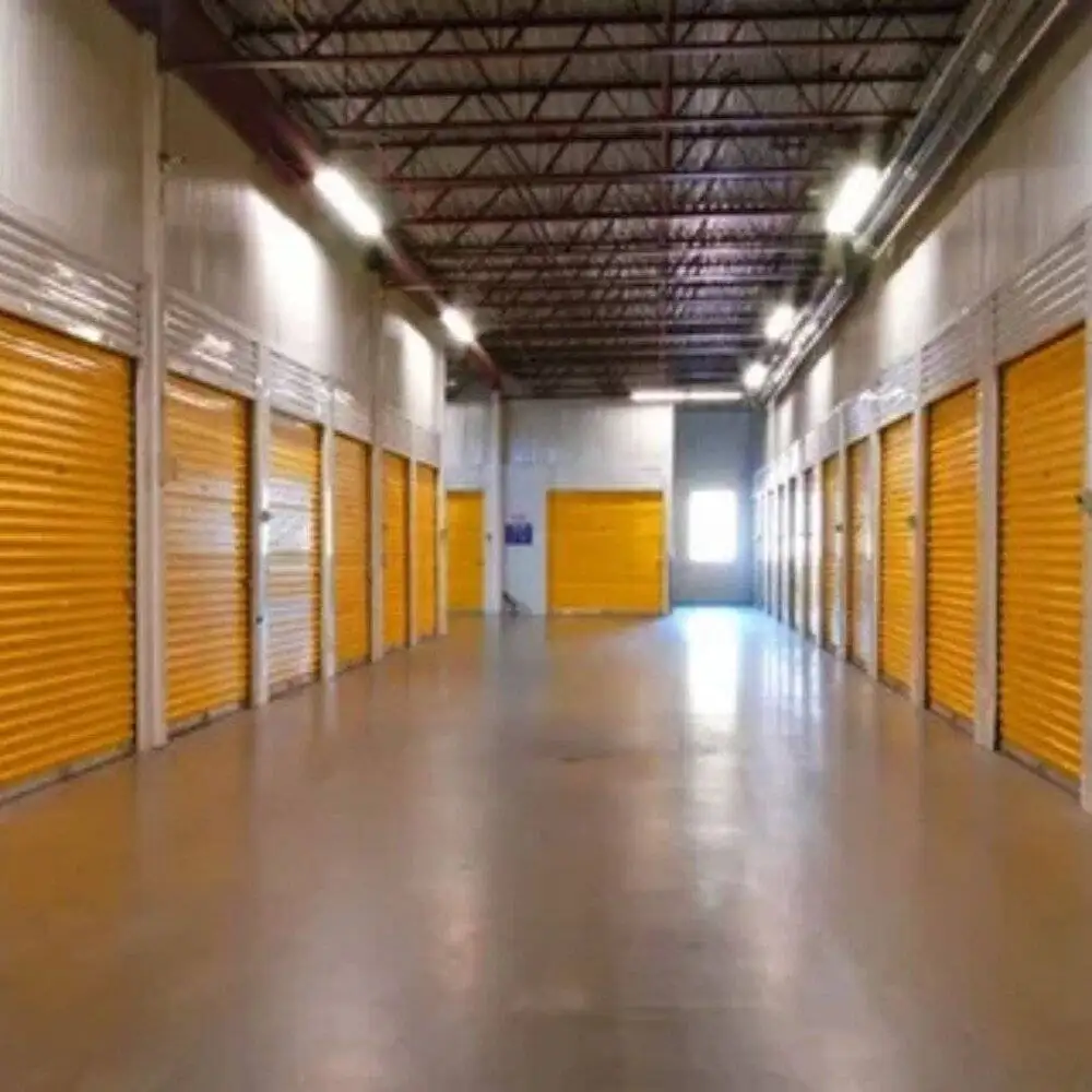 Spacious indoor self-storage facility featuring clean units with bright yellow roller doors. Well-lit hallway ensures easy access and secure storage.