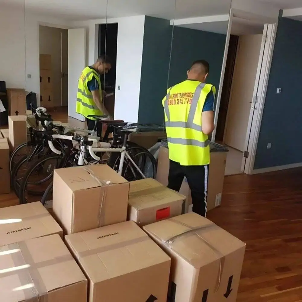 Two team members of 24/7 Movers Packers Storage London are standing near the packed boxes and bicycles ready for relocation