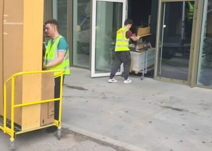Two team members of 24/7 Movers Packers London one is standing with a trolley full of packed boxes and other is carrying trolley into the house/flat/room