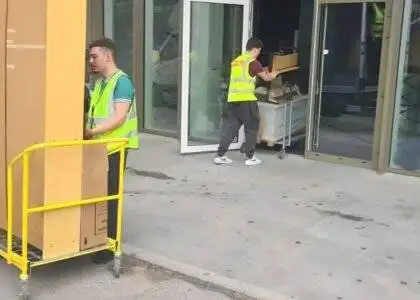 Two team members of 24/7 Movers Packers London one is standing with a trolley full of packed boxes and other is carrying trolley into the house/flat/room