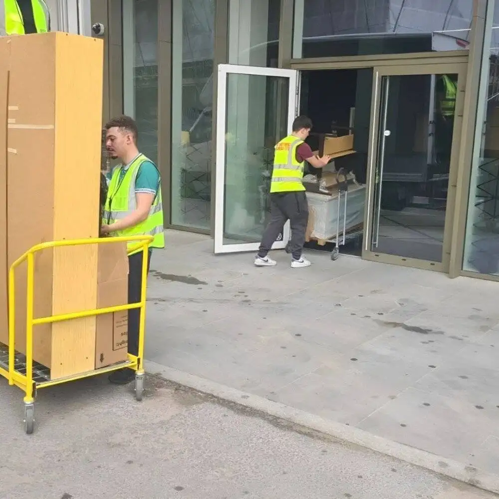 Two team members of 24/7 Movers Packers London one is standing with a trolley full of packed boxes and other is carrying trolley into the house/flat/room